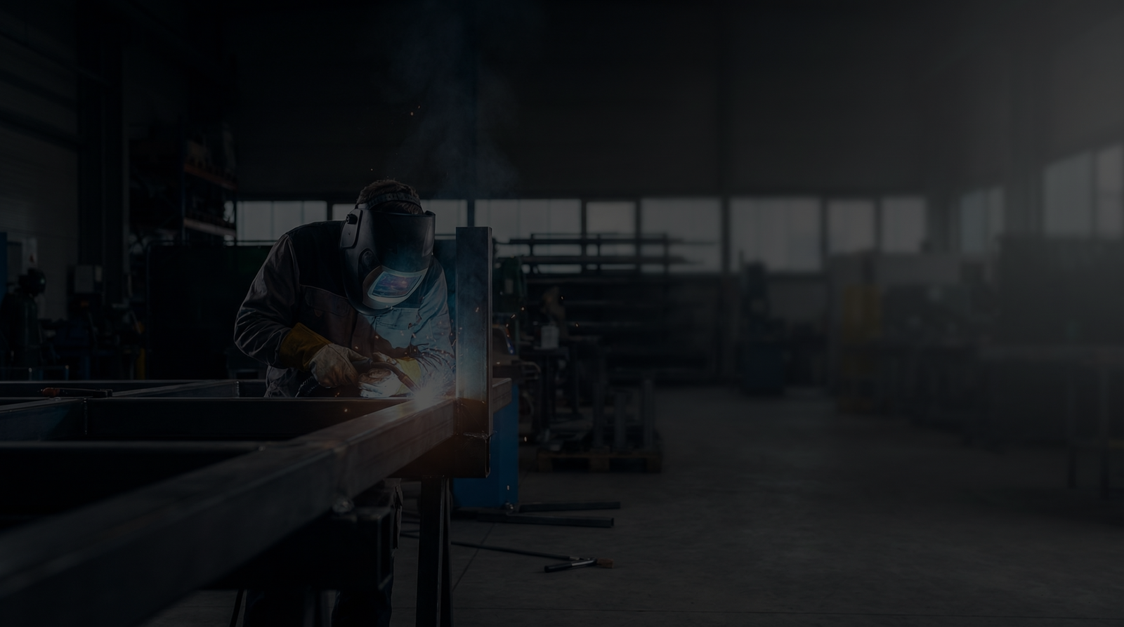 A welder working on a metal structure in a workshop.