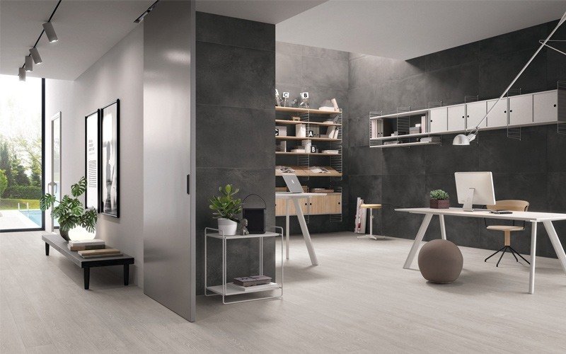 A modern, open-plan office space featuring light grey flooring and dark accent walls with minimalist white furniture and large windows.